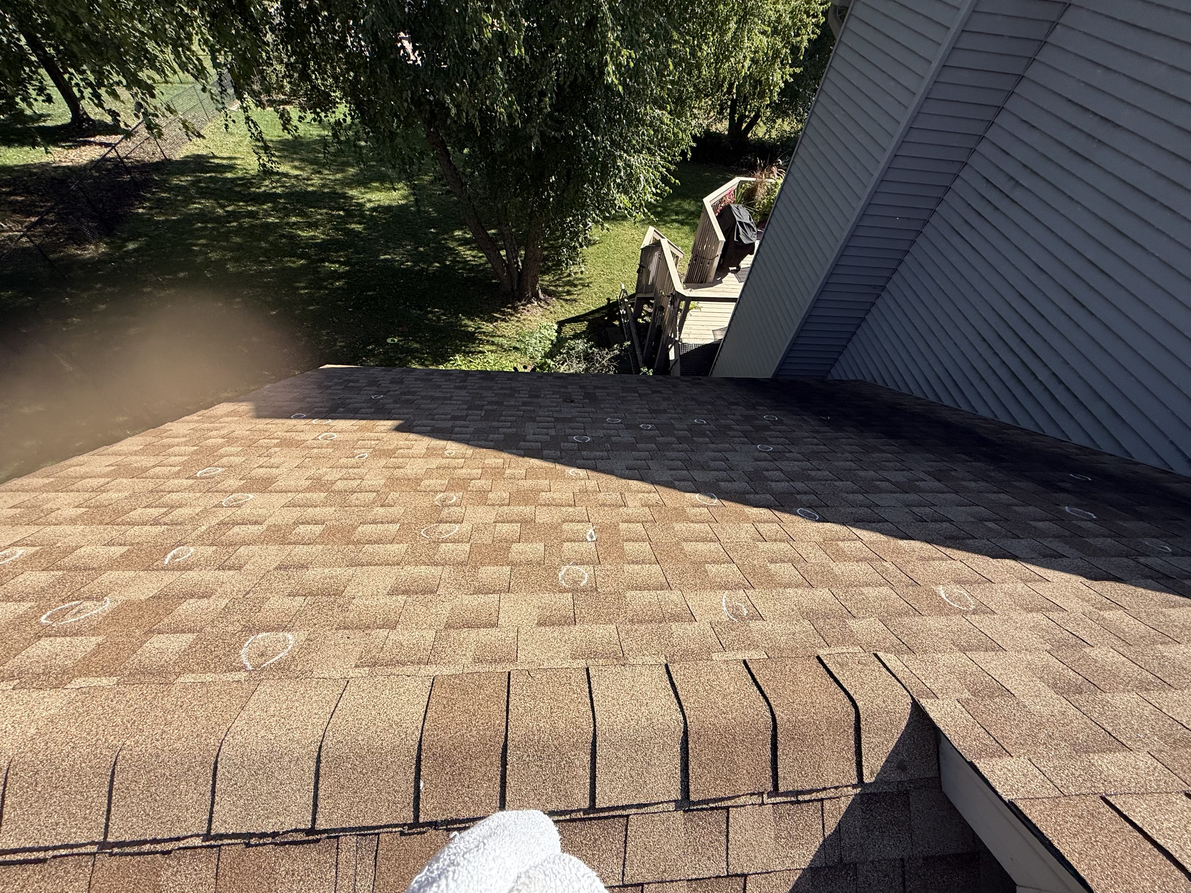Hail-damaged shingles circled across a sloped Burnsville roof near a backyard deck