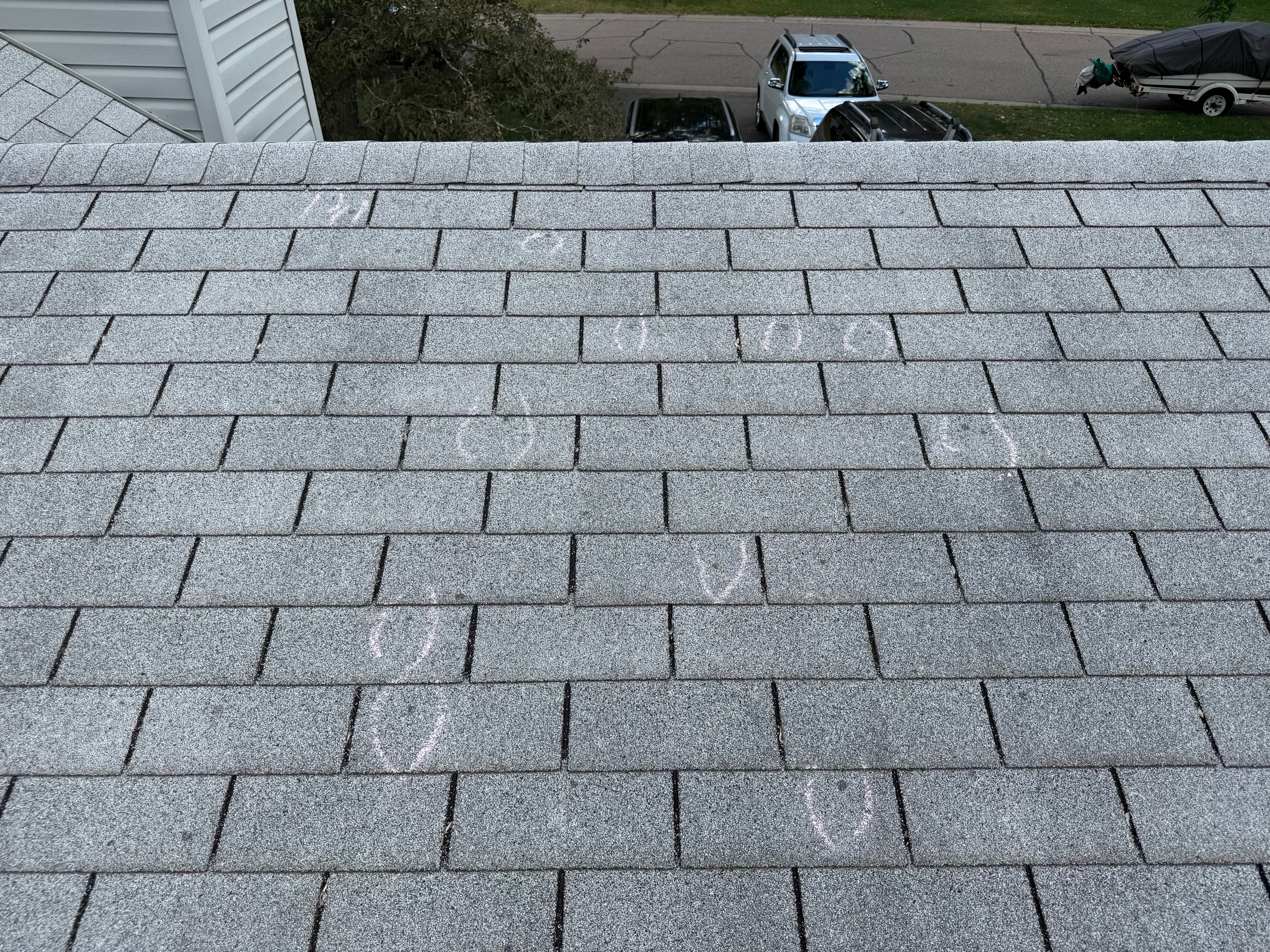 Wide drone-level view of residential roof with multiple hail impacts circled in white chalk