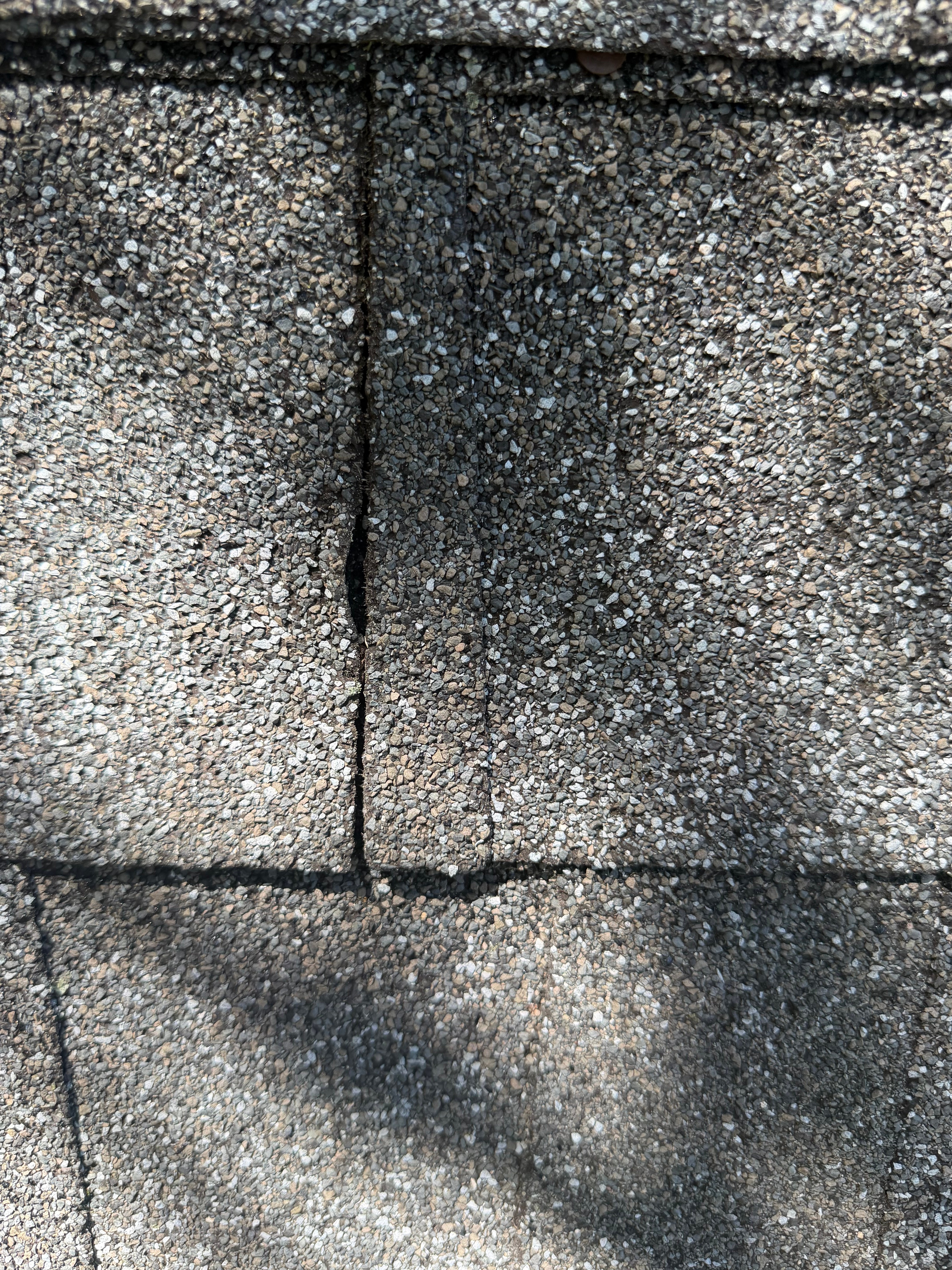 Close-up of shingles showing wind-lifted cracking and splitting along the tab seam
